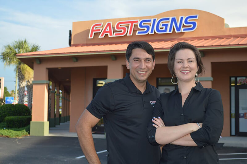 Thiago De Araujo and his wife Julie Fuller stand outside of the FASTSIGNS they own in St. Augustine, FL